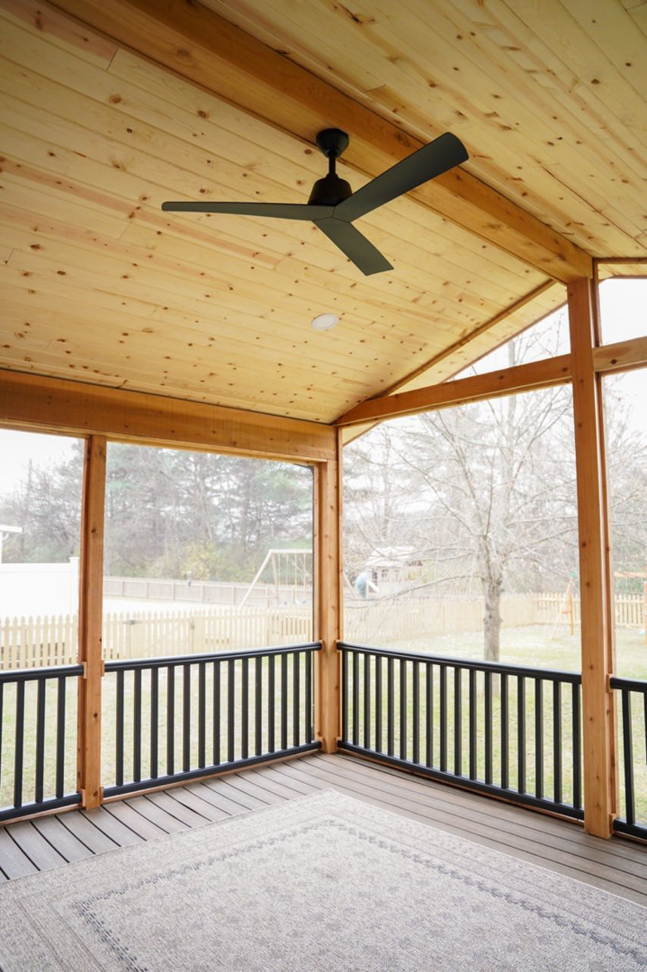The interior of a finished screened porch featuring a ceiling fan by Vision Construction in Framingham, MA.