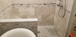 A detailed view of a finished tiled shower with a built-in bench and hexagonal floor tiles by Raleigh Renovations & Flooring in Cary, NC.