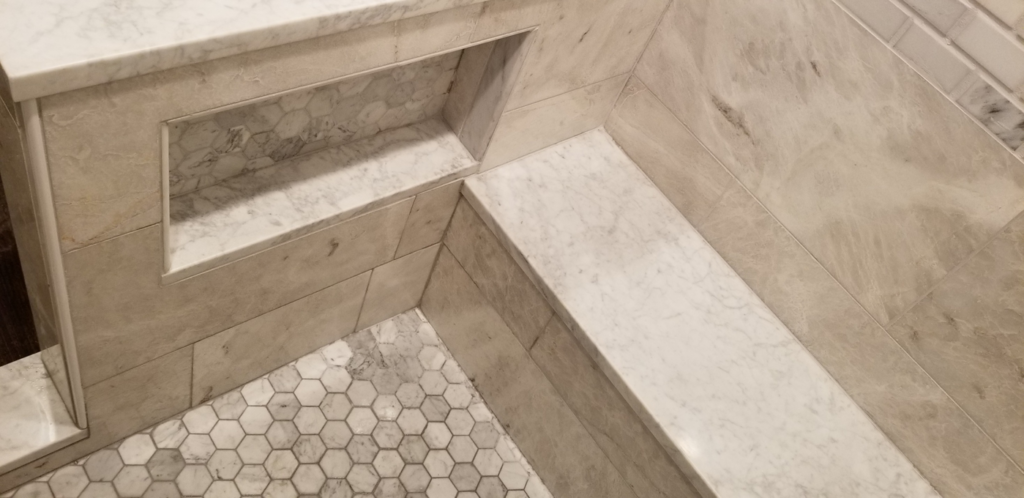 A close-up of a finished tiled shower niche and hexagonal floor tiles by Raleigh Renovations & Flooring in Cary, NC.