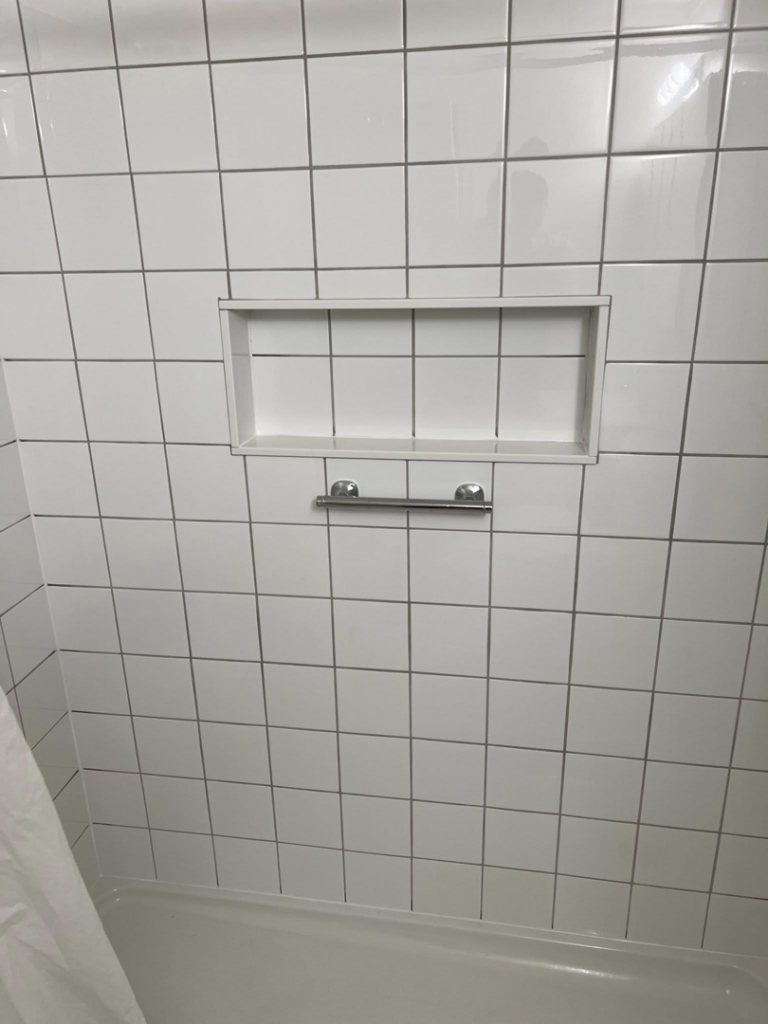 A finished white tiled shower with a built-in niche and grab bar installed by Home Changes in Knoxville, TN