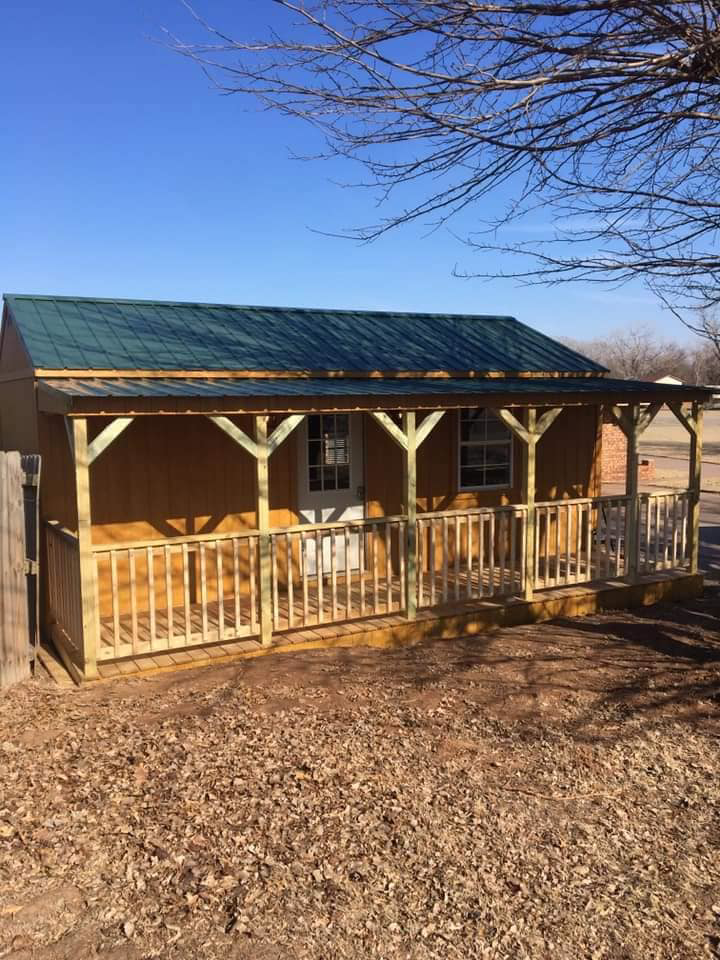A beautifully finished small wooden shed or cabin with a front porch and railing, built by K&K Construction LLC in Enid, OK