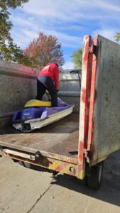 A Fire Dawgs Junk Removal employee stands with a jet ski inside a large junk removal truck in Bloomington, IN.