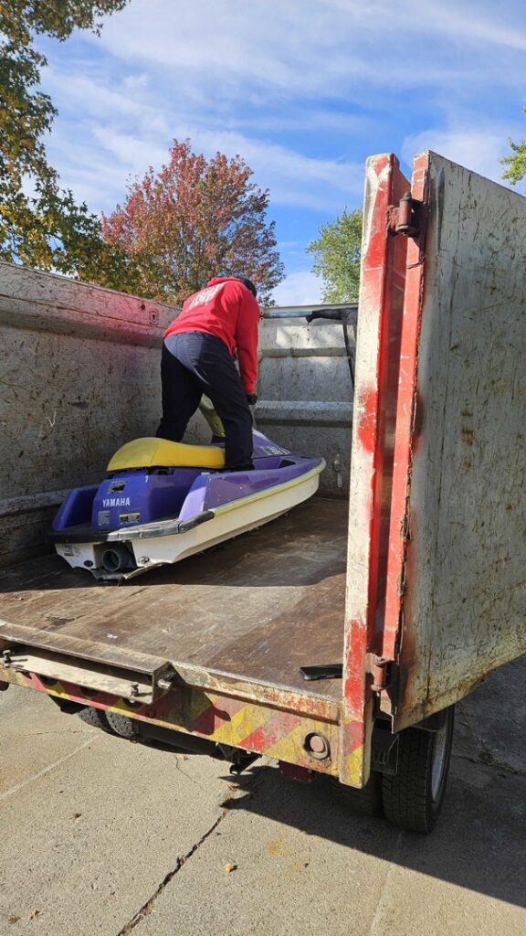 A Fire Dawgs Junk Removal employee stands with a jet ski inside a large junk removal truck in Bloomington, IN.