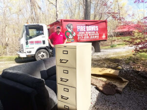 A Fire Dawgs Junk Removal employee stands by their truck with a couch and filing cabinet ready for removal in Bloomington, IN.