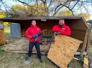Two Fire Dawgs Junk Removal employees stand in front of a partially demolished shed, ready for debris removal in Bloomington, IN.