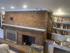 A brick fireplace and built-in shelves taped off and prepped for painting by Carolina Handyman Builder in Taylors, SC.