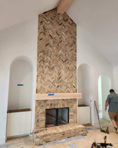 Handyman constructing a brick fireplace with a wooden mantel at a home in Opelika, AL by Homeworks of Alabama, Inc.