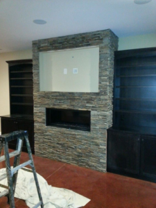 A custom fireplace and entertainment center build with stacked stone and built-in shelves by Cliff's Construction in Richmond, VA.