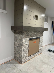 A newly installed fireplace with stone veneer and a modern shiplap surround by Tri Lake Construction in Madison, WI
