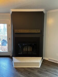 A renovated fireplace with a new wooden mantel and dark accent wall by Lynden Remodeling in Cincinnati, OH.