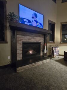 A renovated fireplace with a brick surround, wooden mantel, and TV mounted above by Halpin Hands in Williams, OR.