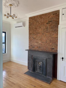 Renovated room featuring a restored brick fireplace and a new chandelier installation by MTI Carpentry in Jersey City, NJ.