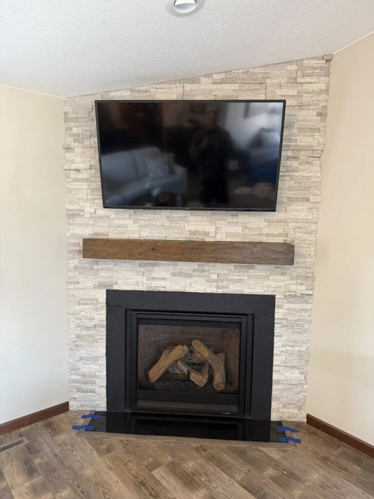 Custom fireplace with stone veneer, wooden mantel, and mounted TV, completed by Watertown Handyman in Watertown, SD.