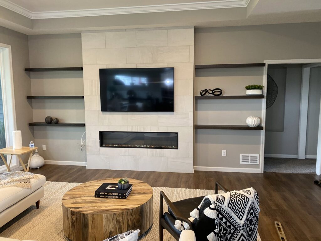 A living room featuring a newly tiled fireplace surround, mounted TV, and installed floating shelves by Clear Choice Handyman LLC in Woodbury, MN.