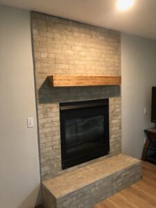 A newly installed fireplace tile surround with a wooden mantel by CSR Tile Construction LLC in Minneapolis, MN.