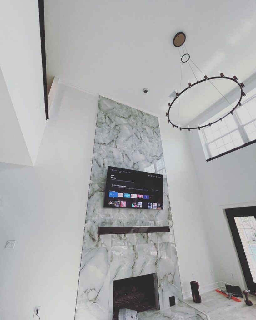 A renovated living room featuring a tall fireplace with a marble-look tile surround and a modern chandelier by J.C.Improvement in Katy, TX.