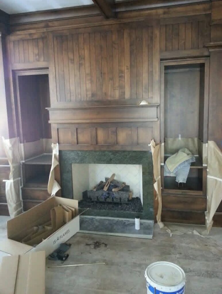 A fireplace installation with a wooden mantel and surround, showing work in progress by Infinite Fire Features in Colorado Springs, CO.