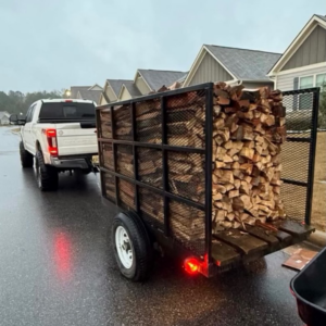 A pickup truck towing a trailer filled with cut firewood, likely for delivery or hauling by Hall's Tree Service in Paw Paw, MI.