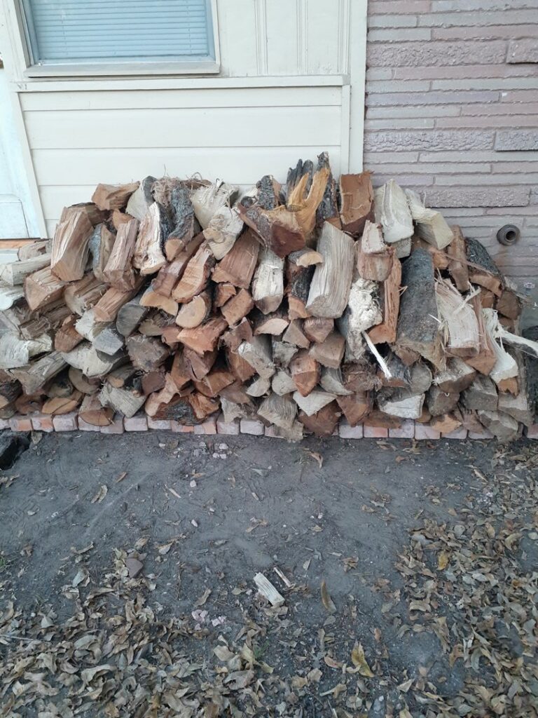 Neatly stacked firewood against a house wall, supplied by Personal Touch Tree Service in Dallas, TX