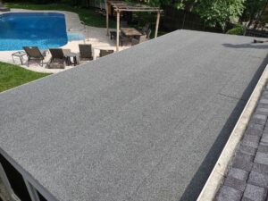 A newly installed flat roof with dark gray material, adjacent to a swimming pool, by Enjaycee Unlimited in Cincinnati, OH.