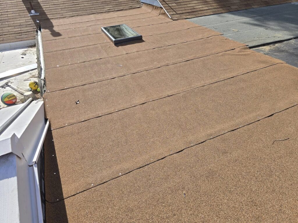Installation of a flat roof with a skylight, showing the new brown granular roofing material by Tillman's Handyman Service in Sparks, NV.