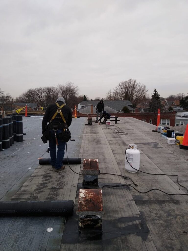 Workers applying new flat roofing material during a commercial roof installation by Pro DK Contractor LLC in Chicago, IL.