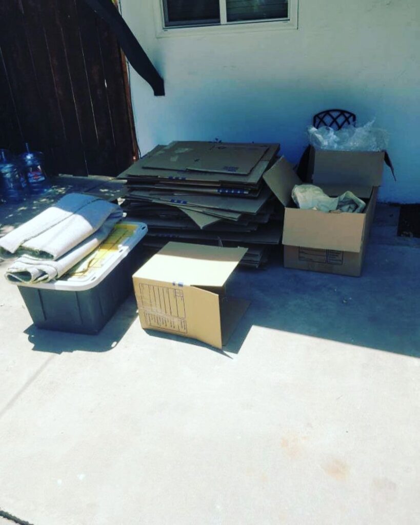 Flattened cardboard boxes and plastic bins stacked outdoors for junk removal by Elite Hauling & Junk Removal in San Diego, CA.