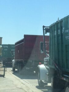 A fleet of junk removal trucks with large containers on a dusty road, operated by A Track-Out Solution in Las Vegas, NV.