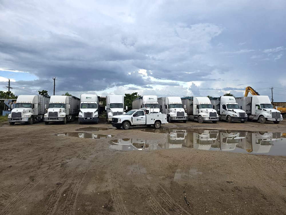 A fleet of large junk removal trucks and an excavator ready for service at Bulk Environmental and Industrial in Miami, FL