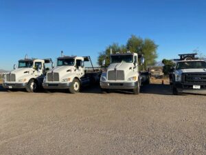 A fleet of white LDI roll-off trucks and a pickup truck parked in a lot for Liberty Disposal, Inc. in Tucson, AZ.