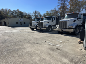 A fleet of three white roll-off trucks parked in a lot at A-1 Roll-Off Rentals, LLC in Baton Rouge, LA.