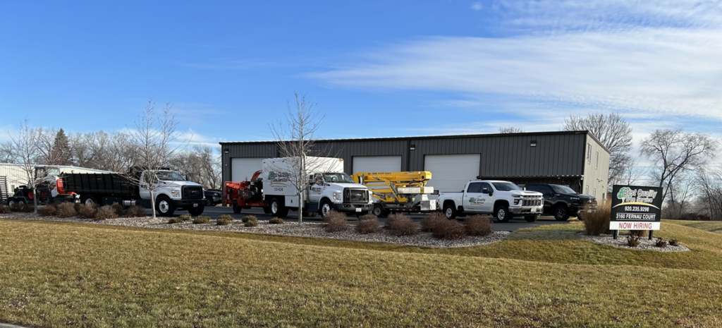 A fleet of tree service trucks and equipment parked outside Best Quality Tree Service in Oshkosh, WI.
