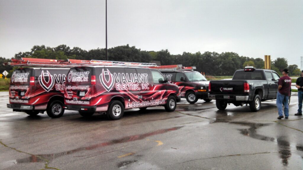 A fleet of Valiant Electric Inc. service vans and a pickup truck parked on a wet lot in Kenosha, WI.