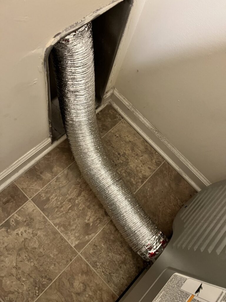 A flexible aluminum dryer vent duct connected behind a dryer, showing the setup for cleaning services in Wilmington, DE.