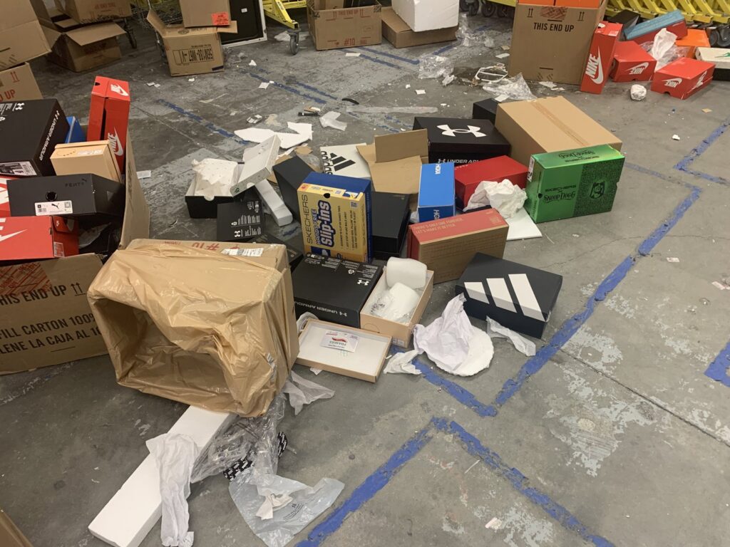 A floor covered with empty shoe boxes and packaging debris, indicating a commercial cleanout job for Roadrunner JunkSmart Solutions LLC in Las Cruces, NM.