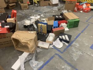 A floor covered with empty shoe boxes and packaging debris, indicating a commercial cleanout job for Roadrunner JunkSmart Solutions LLC in Las Cruces, NM.