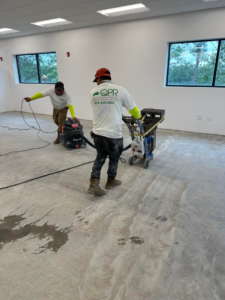 Workers preparing a concrete floor with grinding and vacuuming equipment for Quality Painting of Raleigh in Raleigh, NC.