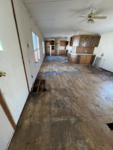 A long room with exposed subfloor and a visible hole, indicating floor repair or renovation work by Cosa Cleanouts & Junk Removal in Topeka, KS.