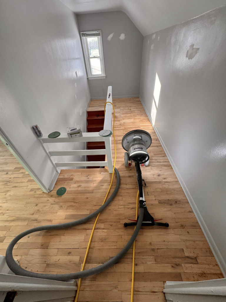 A floor sanding machine with hoses in a hallway, performing a handyman service by Vera Flooring in Grand Rapids, MI.