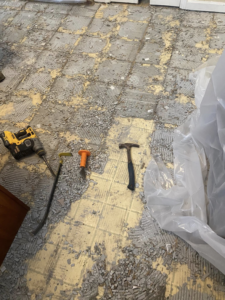 Floor tile demolition in progress with various tools and debris by Main Street Handyman, LLC in Winter Garden, FL.