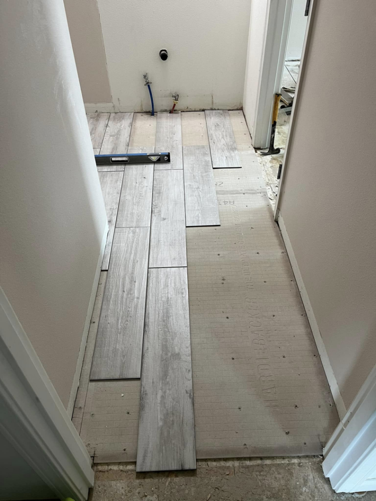 Floor tile installation in progress with a level tool, demonstrating a handyman service by Worths handyman services in Wasilla, AK.