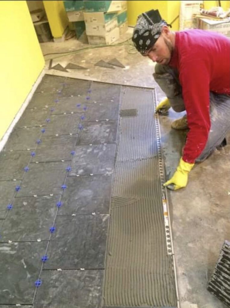 A handyman installing floor tiles, spreading mortar on the subfloor, a service provided by MDJ Handyman in Salt Lake City, UT.