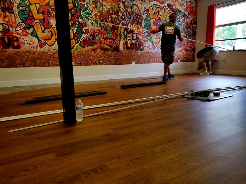 A worker from Stormtroopers Home Improvement installing wood-look flooring in a vibrant commercial space in Port St. Lucie, FL.