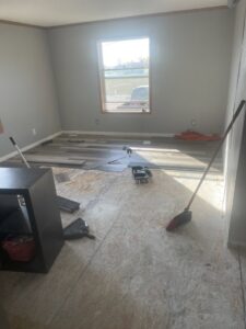 A room with subfloor exposed and new flooring planks laid out, showing a flooring installation in progress by Knutson's Property Maintenance Llc in Williston, ND.