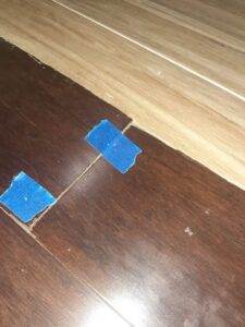 A flooring transition between two different wood-look floors, marked with blue tape, by Glenni Floors LLC in Roswell, GA.