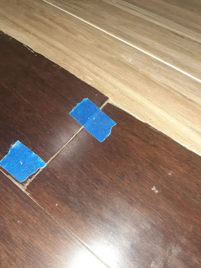 A flooring transition between two different wood-look floors, marked with blue tape, by Glenni Floors LLC in Roswell, GA.