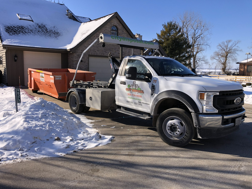 A City Disposal Services Inc. Ford truck delivering an orange roll-off dumpster to a residential driveway in Appleton, WI.