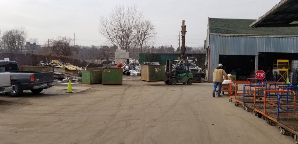 A forklift moving a large dumpster in the outdoor recycling yard at Get Green Recycling Co. in Aurora, IL.