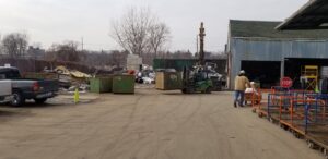 A forklift moving a large dumpster in the outdoor recycling yard at Get Green Recycling Co. in Aurora, IL.