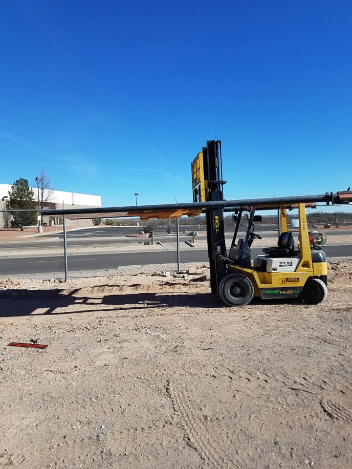 A yellow forklift moving a long metal pipe at the FL Scrap facility in El Paso, TX, demonstrating general junk removal operations.